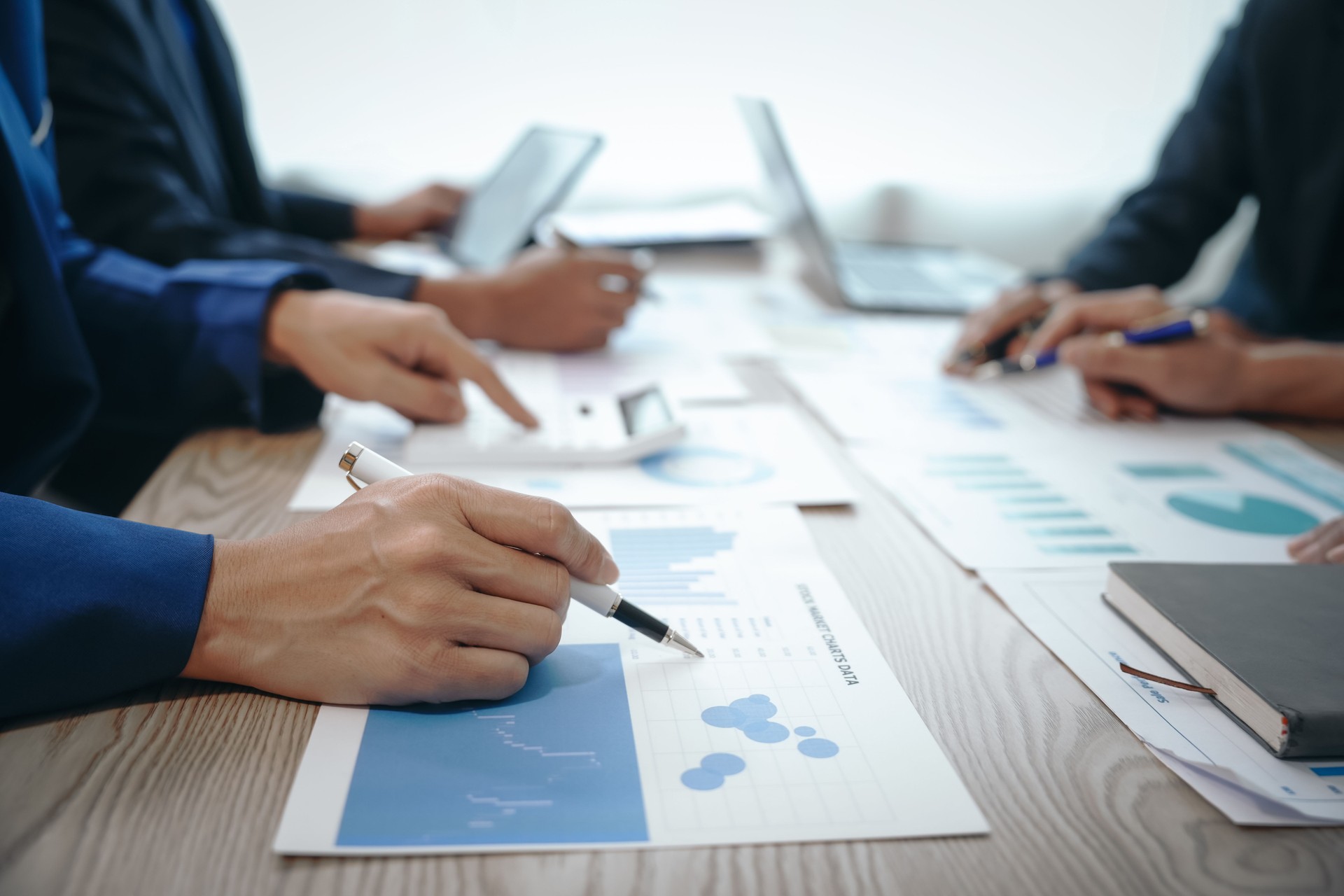 A professional business team meeting in formal suits, working at desks with financial papers, calculators, and laptops. Close-up of hands. Discussion on revenue, brand, sales, agenda, capital